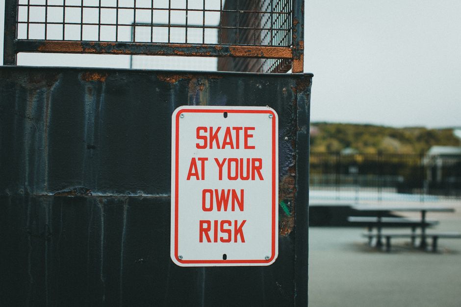 Close-up of a 'Skate at Your Own Risk' sign at outdoor skate park.