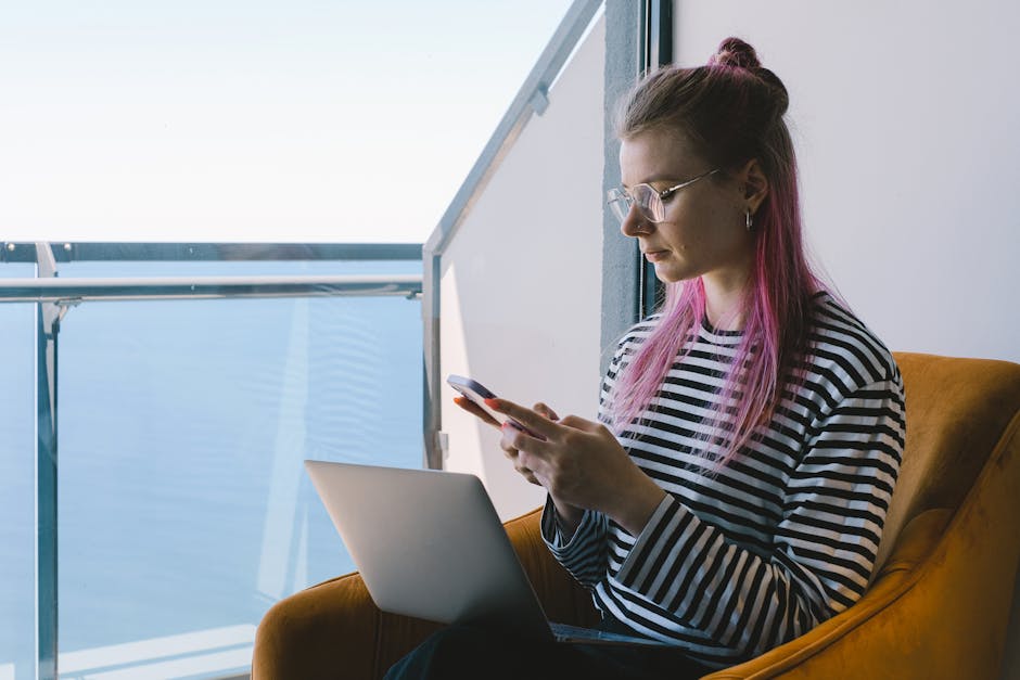 Young woman working remotely, using laptop and phone, enjoys sea view.