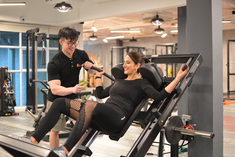 A personal trainer helps a woman with leg presses at a modern gym in Singapore.