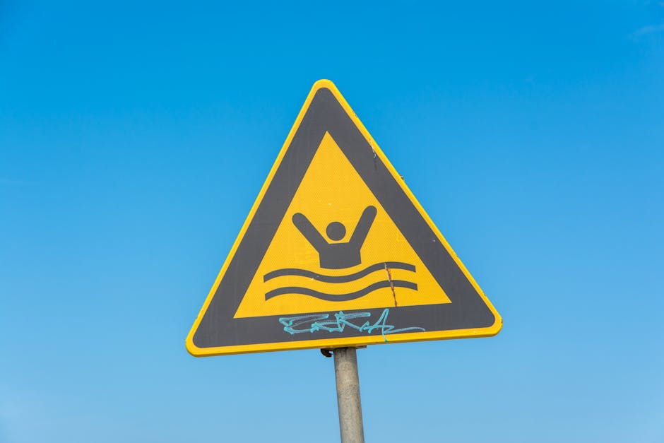 Yellow triangular warning sign for swimming area under a clear blue sky.