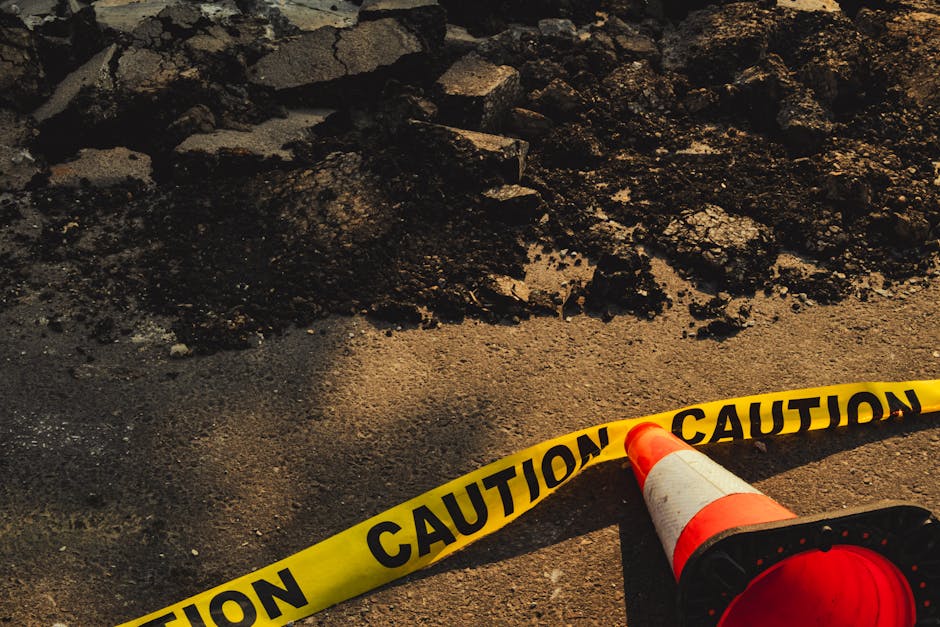 Broken sidewalk with rubble, caution tape, and traffic cone in urban construction site.