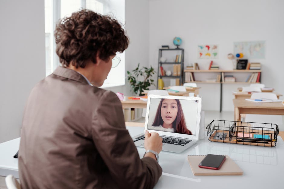 A teacher engages in an online class from an empty classroom, using a laptop for learning.