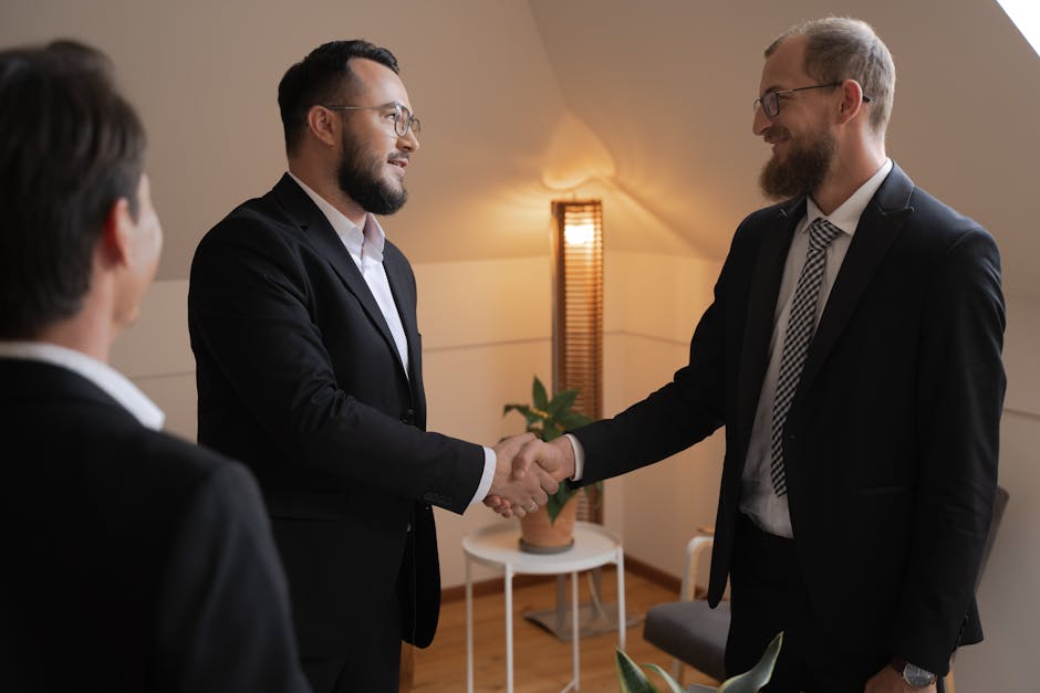 Two businessmen in suits shaking hands in a warm office setting.