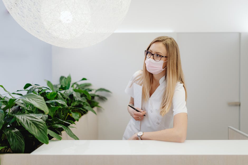 A female healthcare worker in a clinic wearing a face mask, standing at the reception desk.
