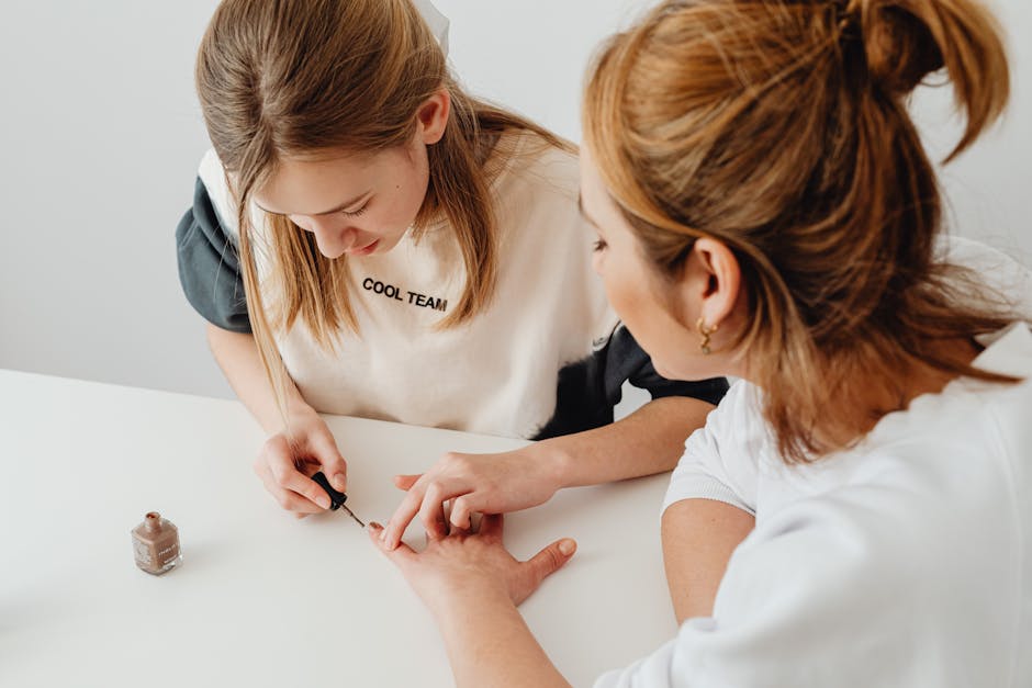 A young woman performs a manicure on another in a well-lit room, showcasing nail care and beauty.