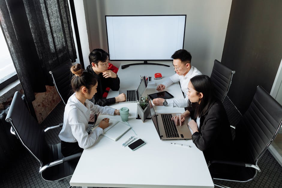 Four professionals collaborating over laptops in a bright, modern office space.