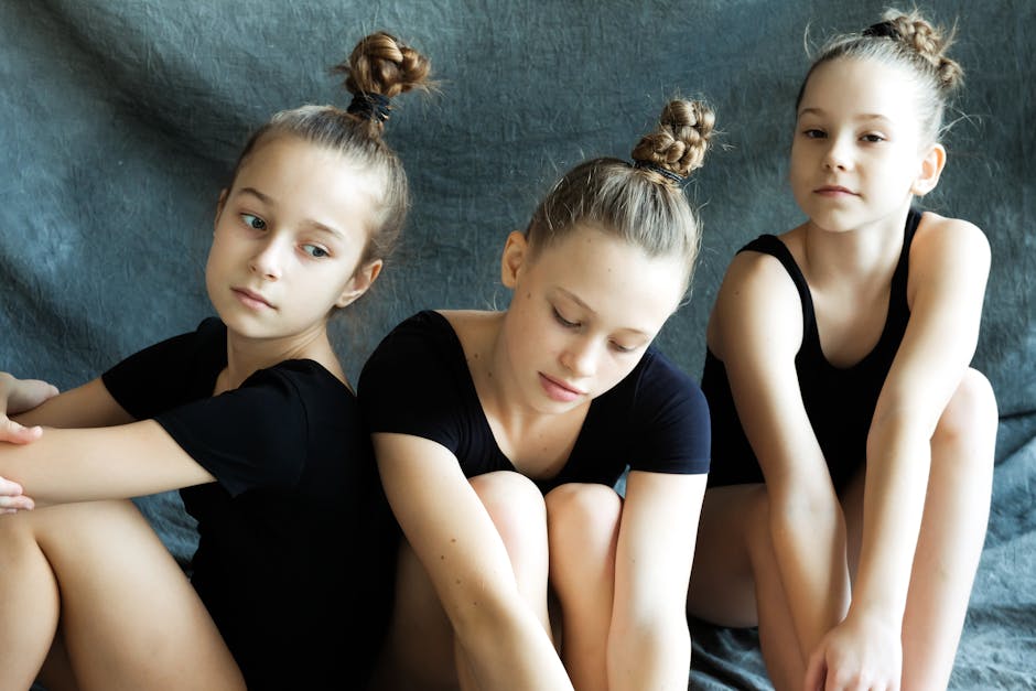Three young ballerinas in black outfits sitting together on a textured background.