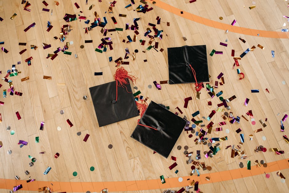 Three black graduation caps and vibrant confetti scattered on a wooden gym floor.