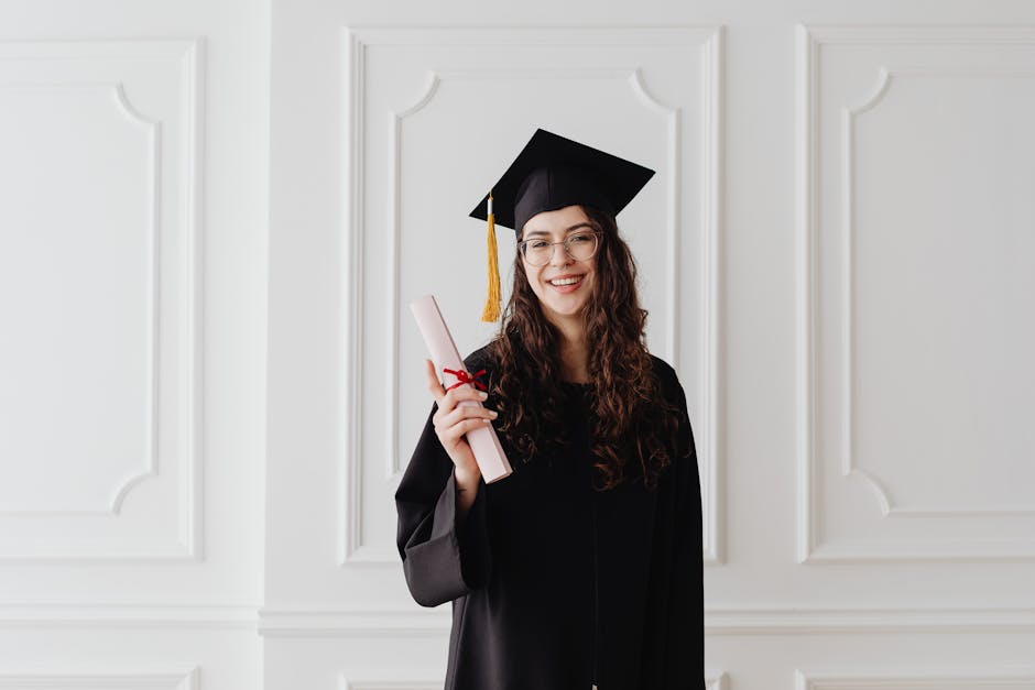 Smiling young woman in graduation gown and cap holding a diploma indoors.