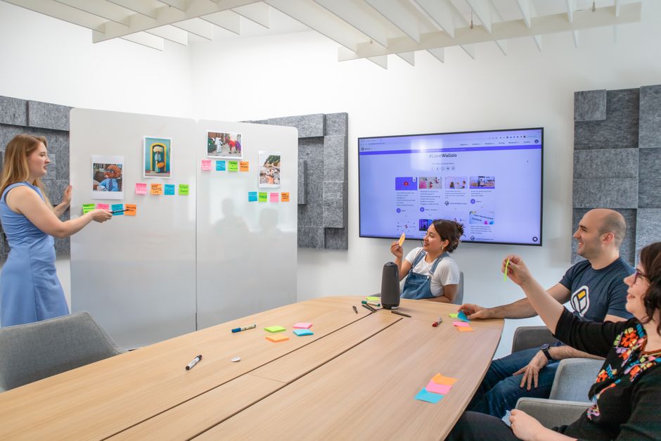 A group of people in an office setting collaborating with sticky notes on a whiteboard.