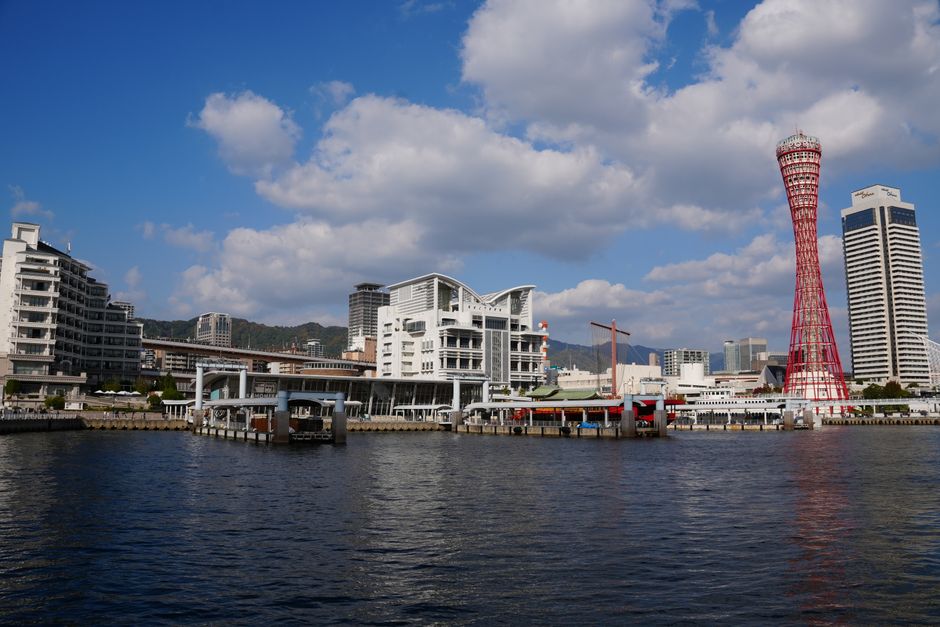 Beautiful waterfront view of Kobe Harbor with iconic red Kobe Port Tower under blue skies.