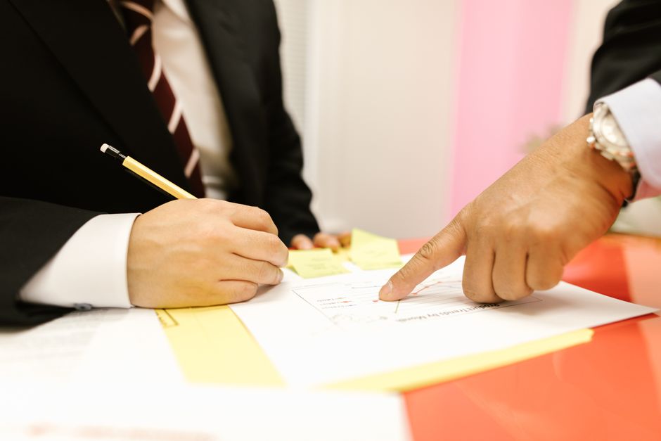 Close-up of two professionals in a meeting, reviewing documents with a pen and paper.