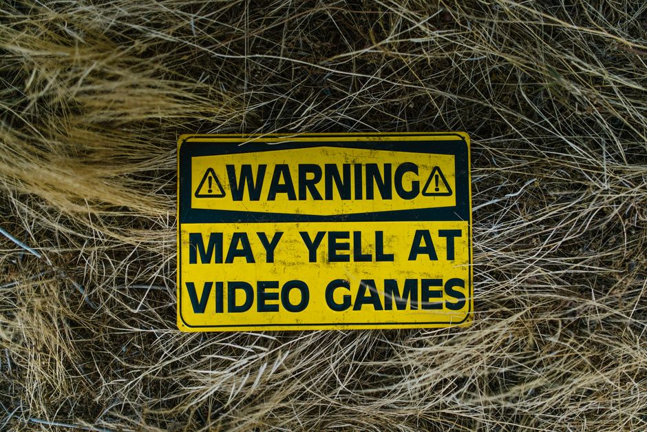 A funny yellow warning sign on grass reading 'Warning May Yell at Video Games'.