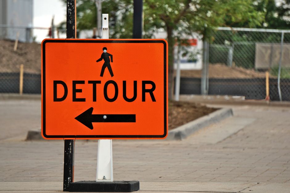 Bright orange detour sign with pedestrian icon guides street traffic.