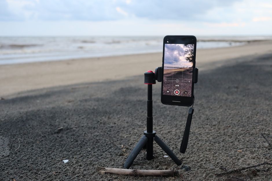 A smartphone on a tripod recording a serene beach setting, capturing the coastal beauty.