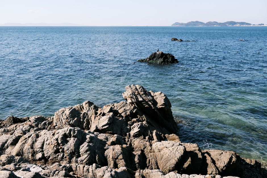 Stunning rocky seashore in Gamagori, Japan with clear blue ocean and distant islands.