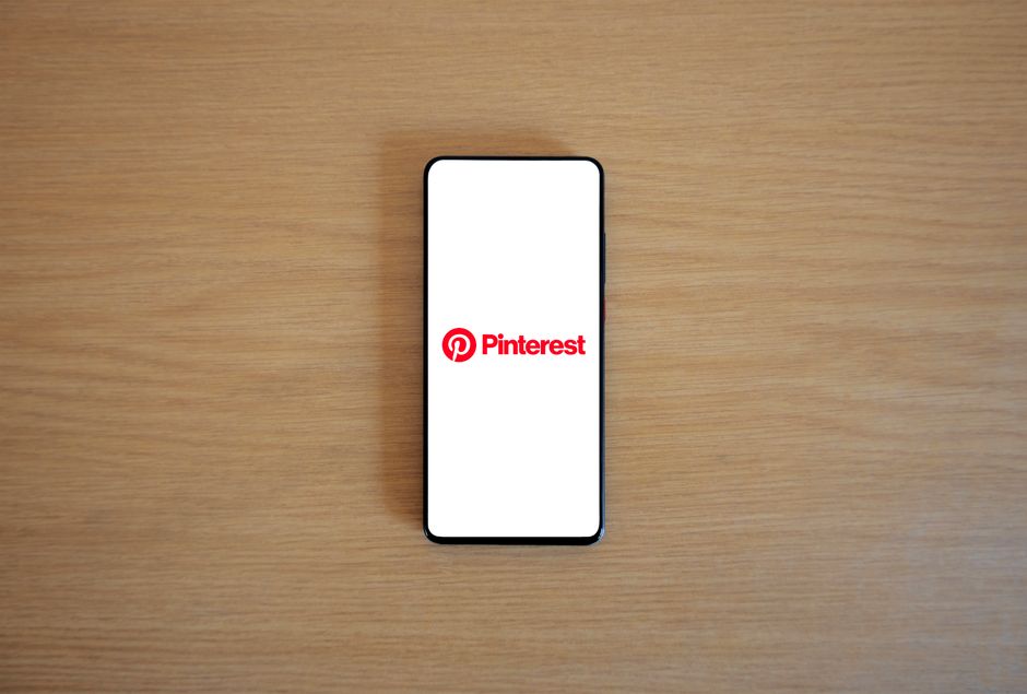 Smartphone with Pinterest logo on screen placed on a wooden surface, minimalistic tech concept.