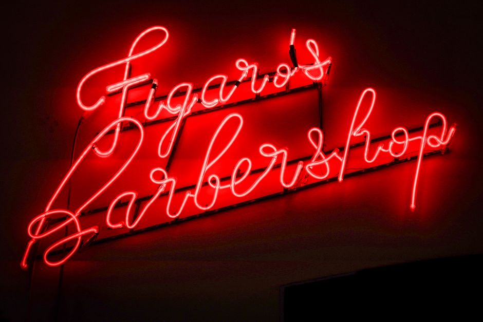 Red neon figaro's barbershop sign glowing at night in Lisbon, Portugal.
