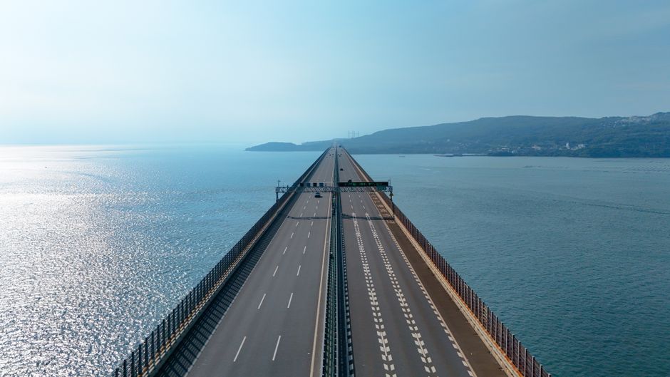 A scenic view of a long bridge stretching over the ocean with blue skies.