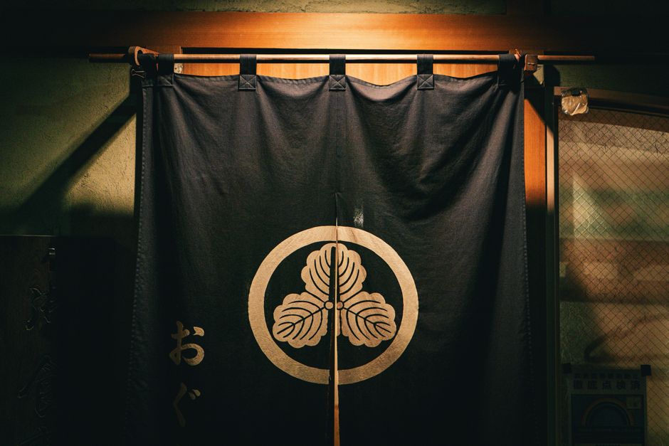 A traditional Japanese noren curtain featuring a mon symbol, hanging in an indoor setting.