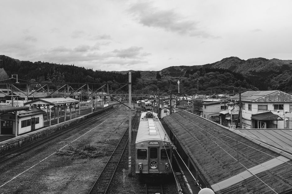 A vintage black and white photo of a rural train station with a scenic mountain backdrop.