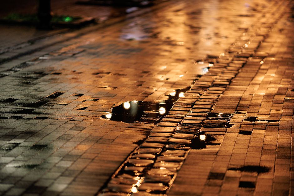 Moody night scene of rain-soaked cobblestones with reflections from streetlights.