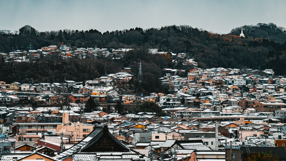 Snow-covered townscape in Japan showcasing traditional architecture and forested hills.