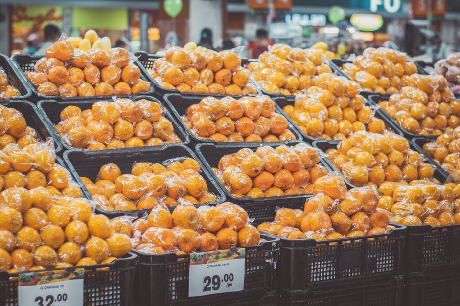 Stack of fresh oranges wrapped in plastic at a grocery store, priced with tags.