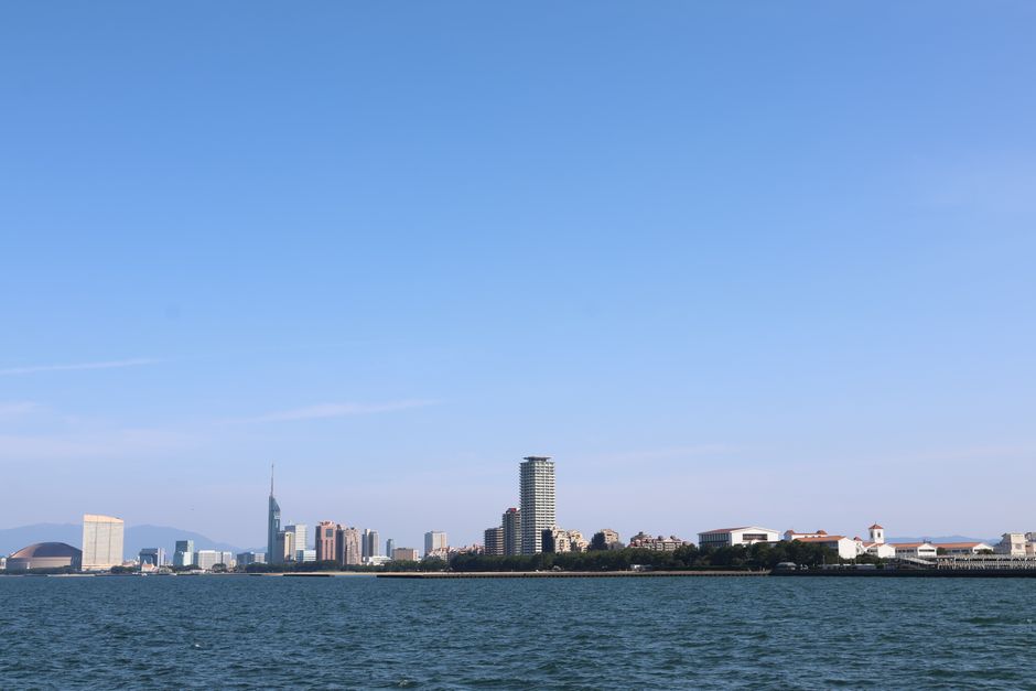 Panoramic skyline of Fukuoka City featuring iconic buildings along the waterfront under a clear blue sky.