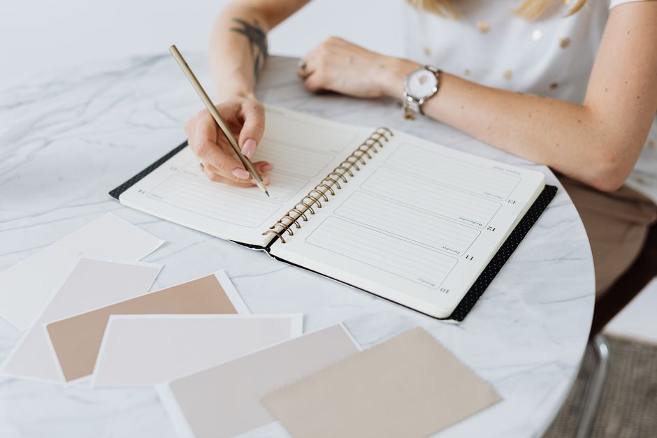 A woman writes in a planner on a marble table, surrounded by swatches. Creative and organized workspace.