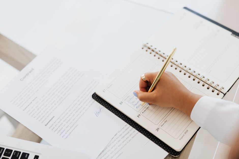 Close-up of a person writing in a planner next to a contract document on a desk.