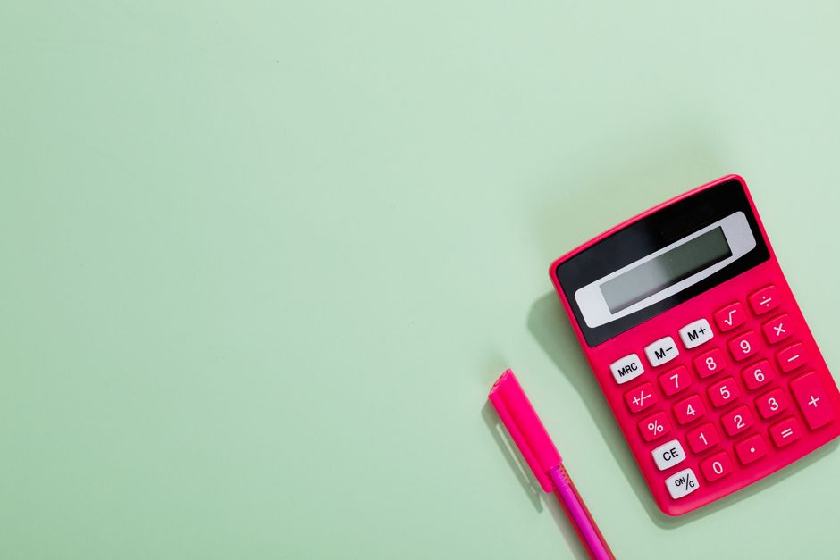 Pink calculator and pen on a pastel green background with copy space.