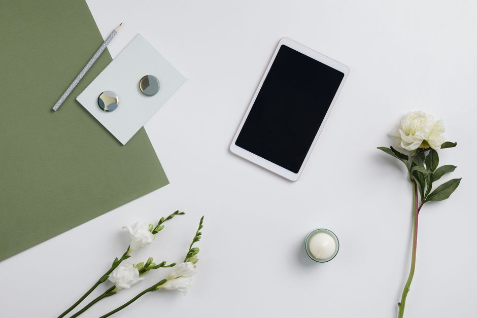 Minimalist composition featuring a tablet, flowers, and stationery on a white background.