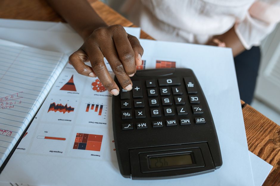 Person using calculator on desk with financial charts and graphs, ideal for business and finance themes.