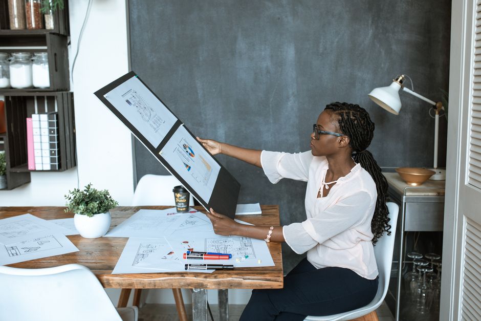 A professional woman analyzes design plans at her workspace, utilizing technology for a creative project.