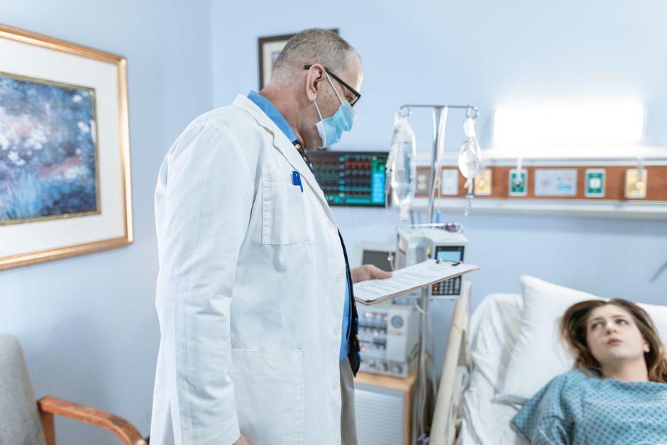 Doctor checks on patient in hospital room with medical equipment.