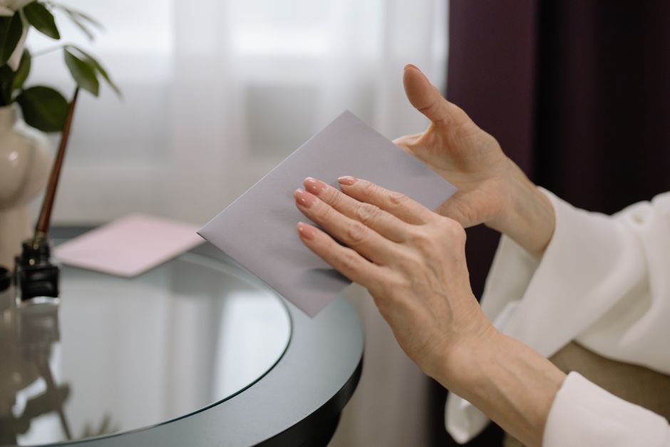 Close-up of hands holding an envelope on a glass table indoors, with a dimly lit room.