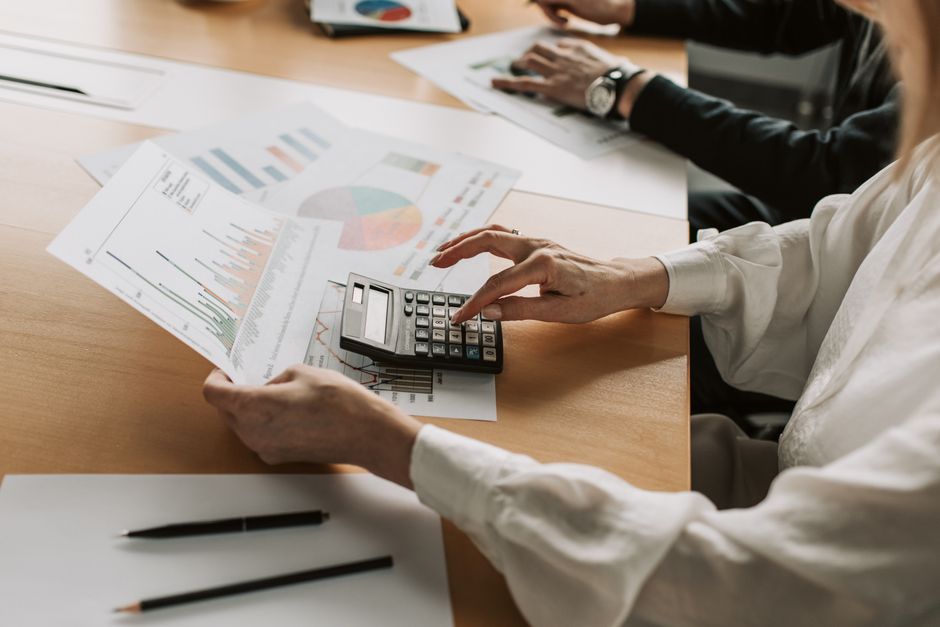 Hands performing financial calculations with charts and a calculator at a meeting table.