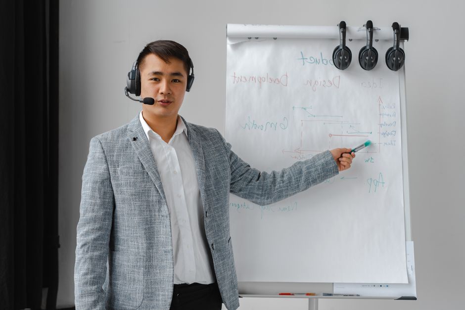 Asian man conducting a business presentation with a headset and flipchart.