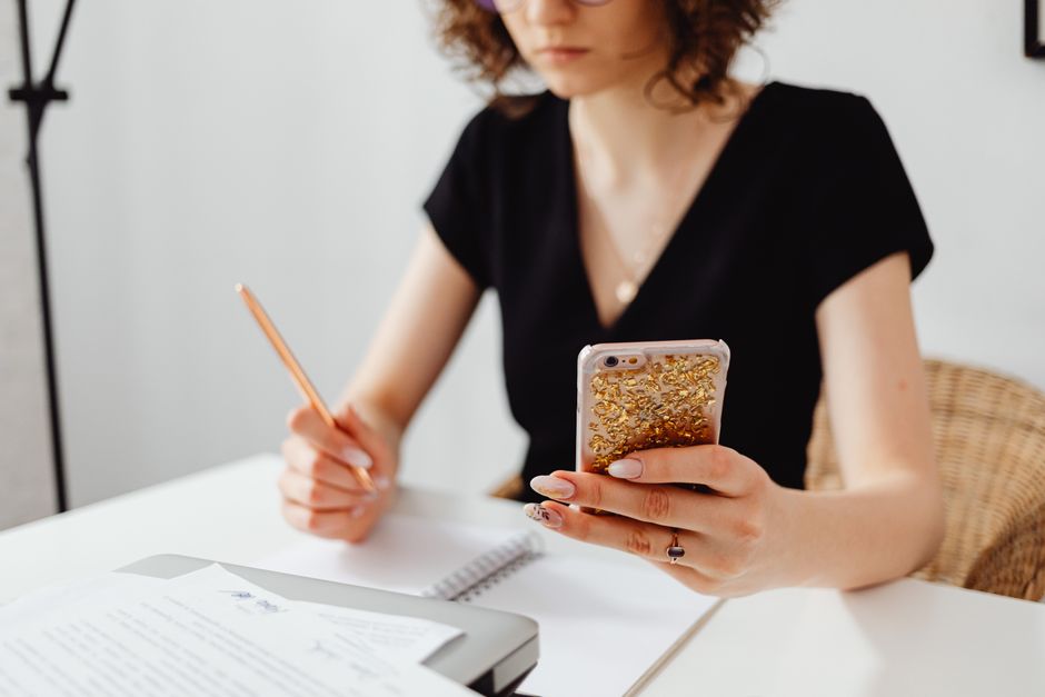 Professional woman multitasking with smartphone and notes at desk in office setting.