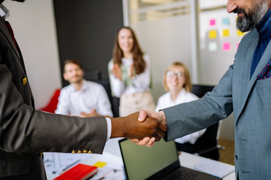 Close-up of a handshake between colleagues in a professional office setting, emphasizing teamwork and agreement.