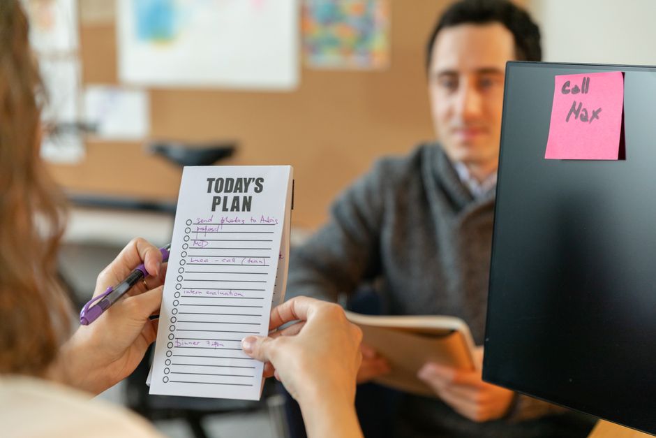 Two colleagues organizing tasks with a plan and sticky notes during a team meeting.