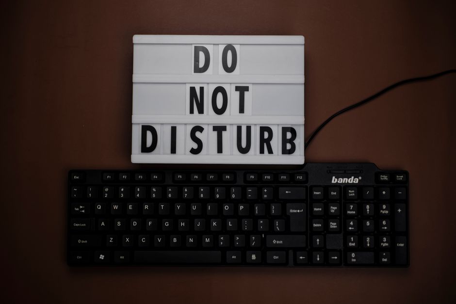 A 'Do Not Disturb' sign above a black keyboard on a brown surface, creating an office atmosphere.