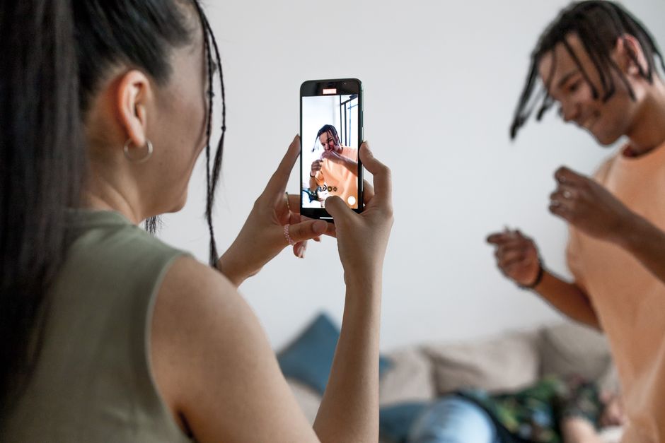 Two friends enjoying a fun, indoor vlogging session, capturing candid moments on a smartphone.