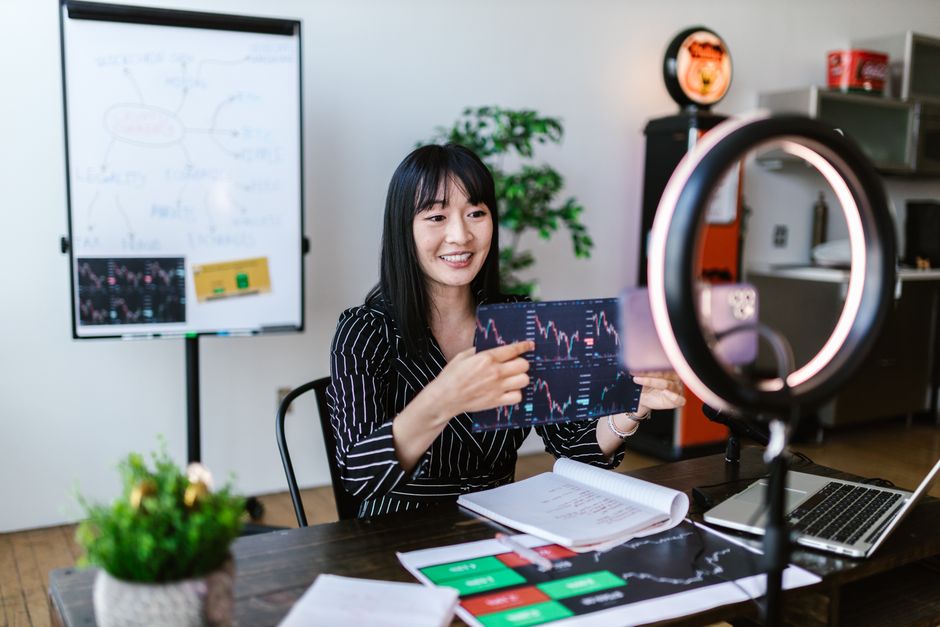 Asian woman discussing cryptocurrency investment during a vlogging session with charts.
