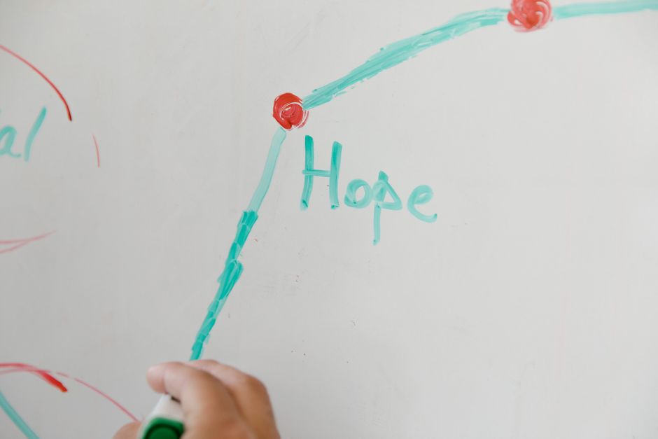 Close-up of a hand drawing on a whiteboard, illustrating hope with colorful markers.